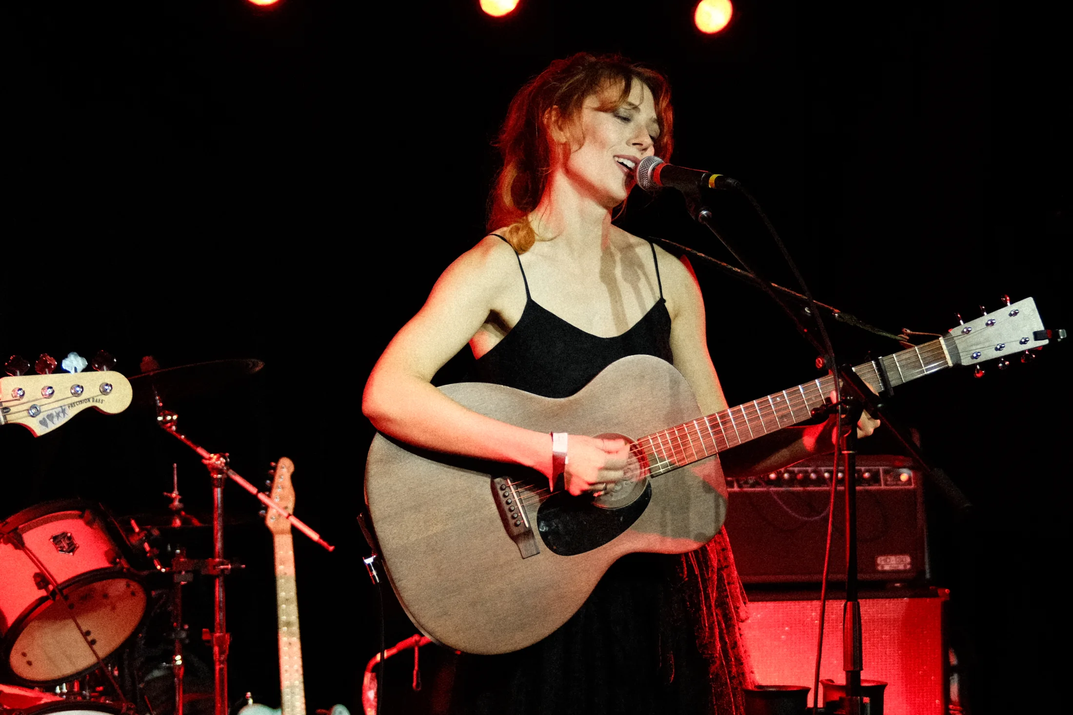 Autumn Cooper performs onstage with an acoustic guitar under red lights.